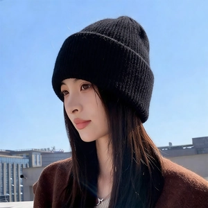Close-up of a double-layered thick black knitted rabbit fur beanie against a blue sky