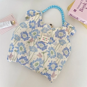 Close-up of floral tote bag with blue woven rope handles and a colorful textile brand tag