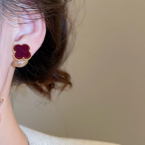 Close-up of model wearing burgundy flocked clover earrings with pearl drop and gold trim
