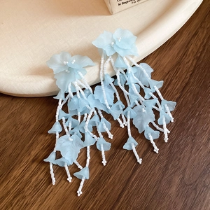 Boucles d'oreilles fleurs en tissu bleu avec glands et perles sur bois rustique