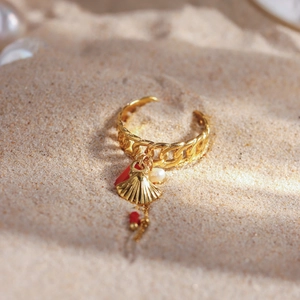 Gold ocean shell charm ring with pearl and coral bead on a sandy beach background