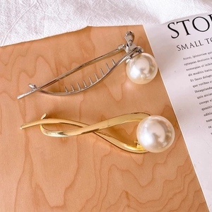Elegant gold and silver hair claws with large white pearls on a wooden display