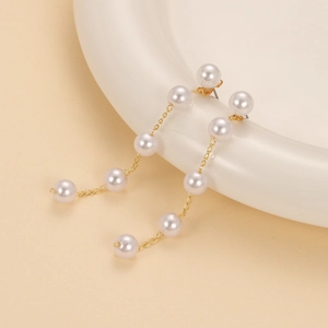 Elegant long gold chain tassel earrings featuring five white faux pearls on a ceramic dish