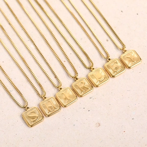 Close-up of gold-plated square initial pendants with Shirley lettering on box chains