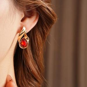 Primo piano dell'orecchino vintage in oro con pietra rossa a goccia indossato dal modello