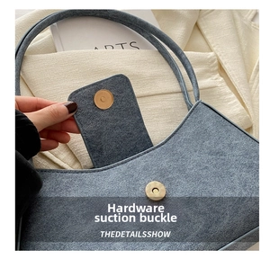 Detail of blue faux suede baguette bag featuring a circular gold magnetic clasp and fine texture