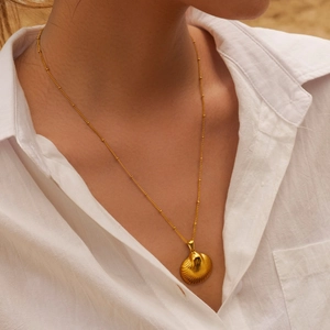 Close-up of a gold shell pendant necklace on a model with a soft beach background