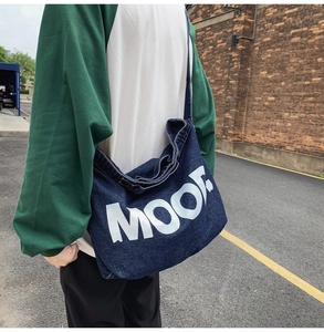 Outdoor lifestyle shot of large denim crossbody bag with white MOO letter print