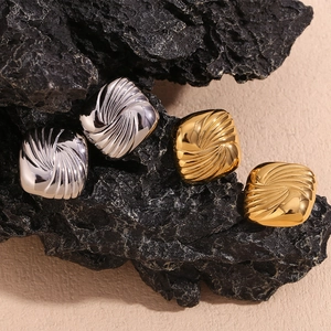 Macro shot of square gold and silver earrings with spiral texture on black rock
