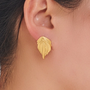 Close-up of a gold feather earring with detailed textures worn by a model