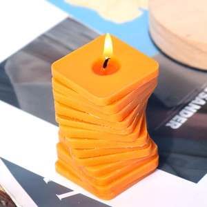 Detalle de una vela de silicona en espiral cuadrada naranja brillante encendida
