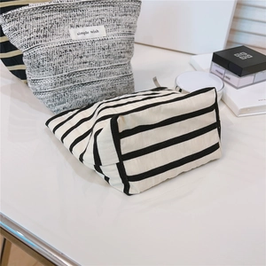 Close-up of striped canvas and tweed cosmetic bags on a white desk with props