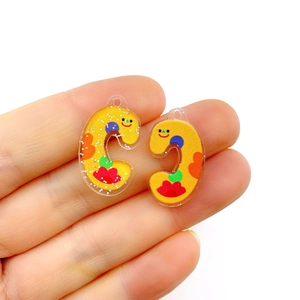 Detailed macro view of a pair of yellow acrylic letter C charms with cartoon smiley patterns