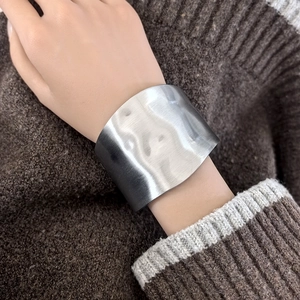 Detail of silver brushed metal cuff bracelet with irregular wavy texture on a model