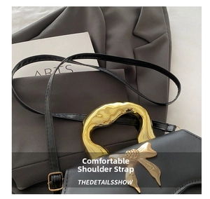 Detail of adjustable black leather strap and metallic bow buckle on fashion handbag