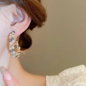 Close-up of multicolor beaded C-shaped hoop earrings worn by a model on a warm background