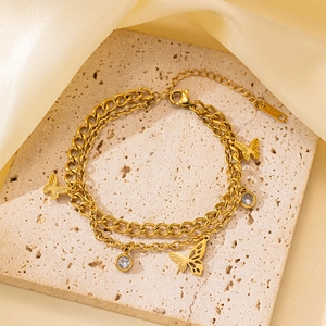 Detalle de la pulsera dorada de doble cadena con dijes de mariposa y cristales finos