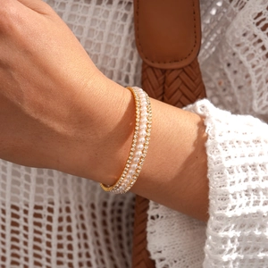 Close-up of a three-row gold bracelet featuring white pearls and sparkling rhinestones