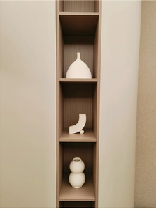 Three minimalist white ceramic vases with unique shapes displayed on a wooden shelf