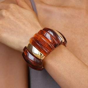 Close-up of chunky amber resin and polished gold metal link bracelet on a wrist