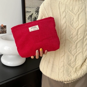 Minimalist red corduroy cosmetic bag held by hand in a cozy home setting