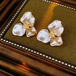 Close-up of white petal stud earrings with gold edges on a vintage velvet base
