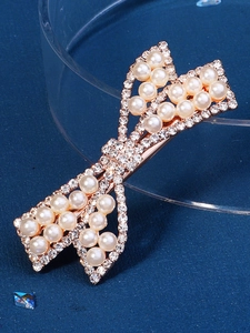 Close-up of golden bow hair clip featuring sparkling rhinestones and elegant pearls