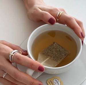Detailed view of layered 925 sterling silver rings worn on model holding a tea cup