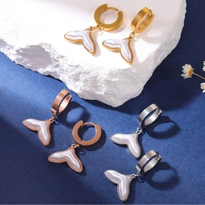 Detailed view of gold, rose gold and silver fish tail pearl earrings on stone base