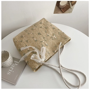 Close-up of woven straw tote bag with green floral embroidery and white lace bow detail