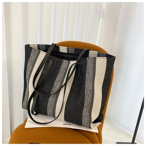 Detail of striped woven tote bag with leather straps on a modern orange stool