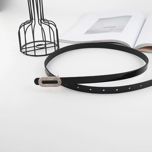 Detail of a thin black patent leather belt with a square rhinestone buckle on a white desk