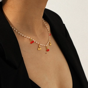 Détail d'un collier de perles avec des pendentifs cerises rouges et dorés sur un mannequin