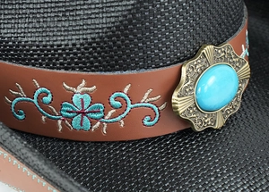 Detail of western cowboy hat with leather band, turquoise embroidery, and metal buckle
