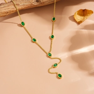 Close-up of gold chain necklace with seven oval green crystal gems on beige background