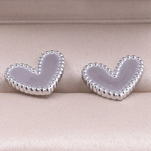 Macro shot of silver heart stud earrings with milgrain edges on a jewelry box cushion