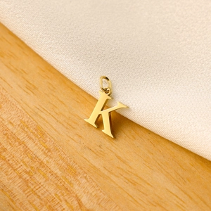 Macro shot of a golden letter K pendant on a white satin and light wood surface