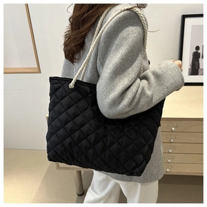Détail d'un sac cabas noir matelassé avec des poignées en corde tressée blanche et œillets