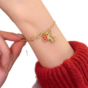 Golden chain bracelet with red coin and puppy pendant on a female model wrist