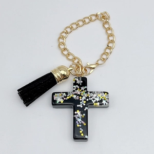 Detailed view of black resin cross charm with colorful sequins and golden tassel chain
