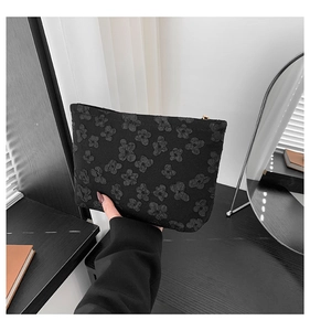 Detailed close-up of a black clutch bag featuring a 3D embossed floral fabric texture
