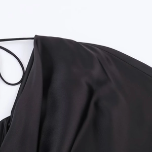 Detailed close-up of a black satin dress featuring thin straps and a draped neckline