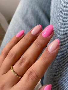 Close-up of long pink and nude press-on nails with gold lines and a gold ring detail