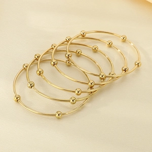 Close-up of five thin gold titanium bracelets with small golden beads on satin