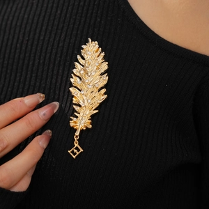 Detail of a golden feather brooch with rhinestones pinned on a black knit sweater