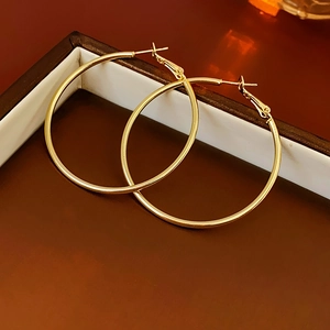 Detail of large gold hoop earrings with smooth metallic finish on dark wooden tray