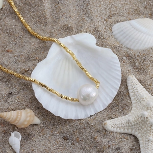 Baroque pearl pendant on a gold beaded silver necklace over a seashell and sand background