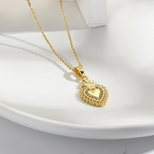 Elegant gold heart pendant necklace with shimmering zircon accents on white ceramic plate