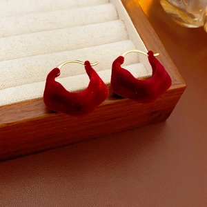Close-up of red velvet heart earrings with gold metal hooks on a wooden display