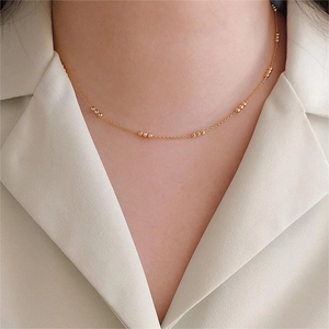 Detail of a minimalist gold beaded chain necklace worn by a model on a cream blouse
